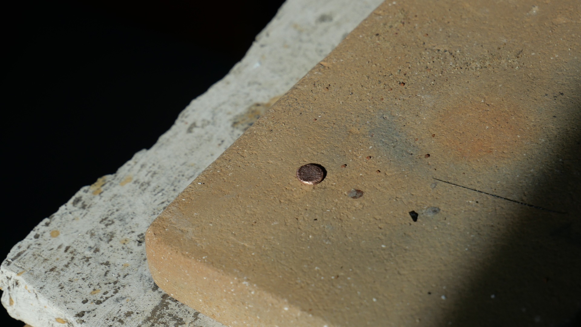 Petit bouton de cuivre métallique obtenu à partir de 250 g de minerai, posé sur brique réfractaire