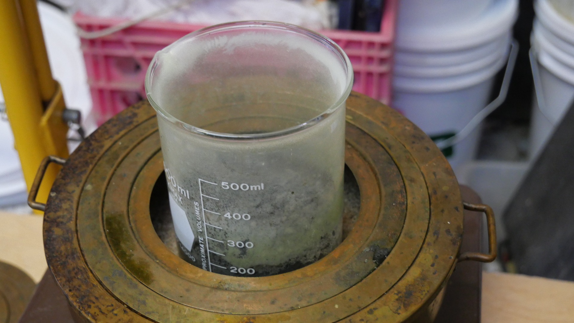 Dépôt pâle de soufre sublimé tapissant la paroi intérieure du bécher au-dessus du résidu de minerai