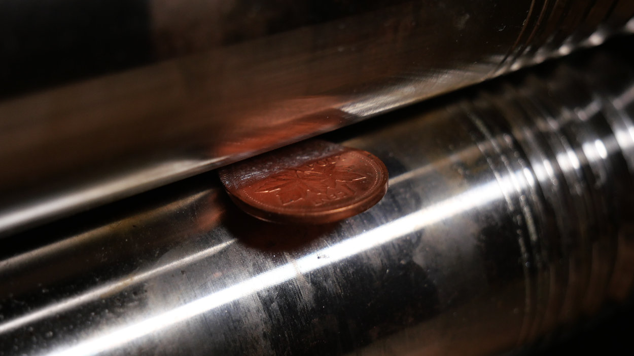 Une cent canadienne calée dans la ligne de pincement des rouleaux d'un laminoir.