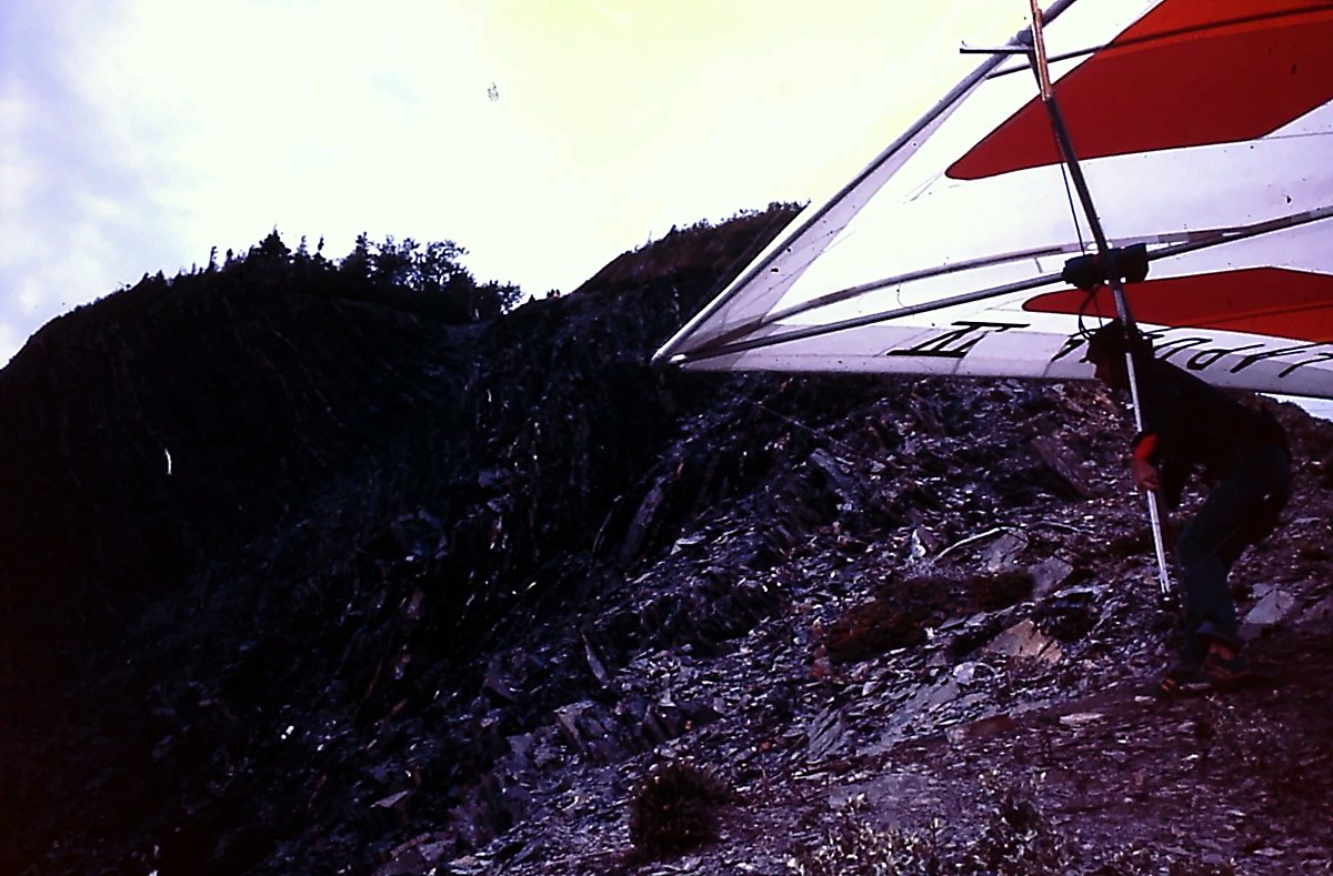 Un pilote penché sous une aile blanche et rouge s'apprête à décoller d'une crête de roches éclatées