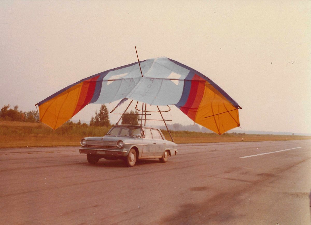 Vue de derrière : la voiture roule sur la piste, l'aile au-dessus d'elle, ses deux bouts relevés et la voile tendue par le vent